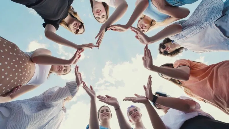 A group of young adults, standing in a circle and joining hands, reflecting teamwork, inclusivity, and shared school values of support and mutual respect.