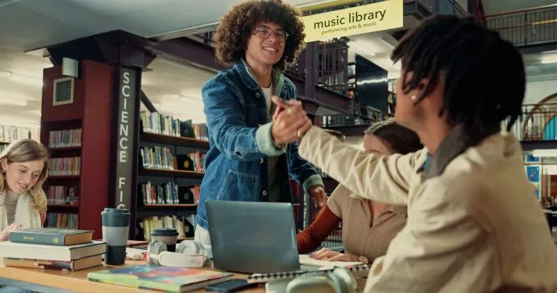 A group of students working together in a school library, engaged in discussion while surrounded by books and educational resources.
