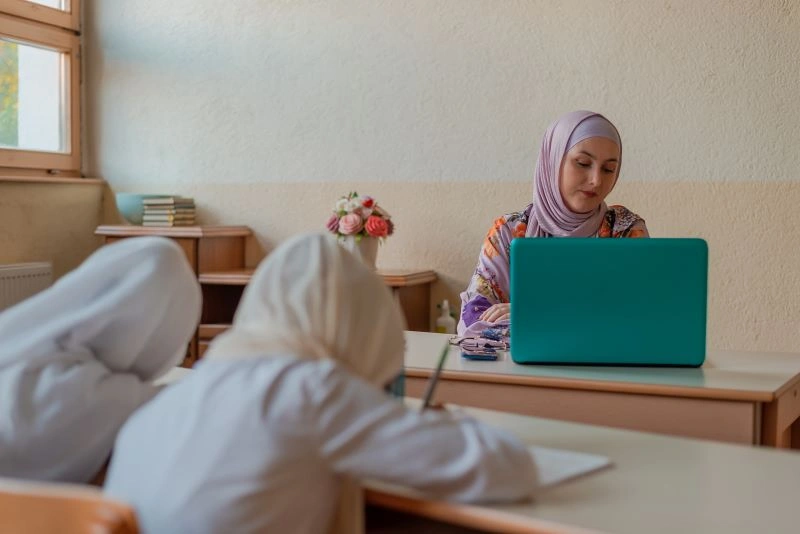 Maintaining focus and discipline in the classroom is essential for effective learning. In this image, the teacher stays engaged with the laptop, leading by example while students focus on their tasks. Discipline ensures a conducive learning environment where students can excel and absorb knowledge effectively.