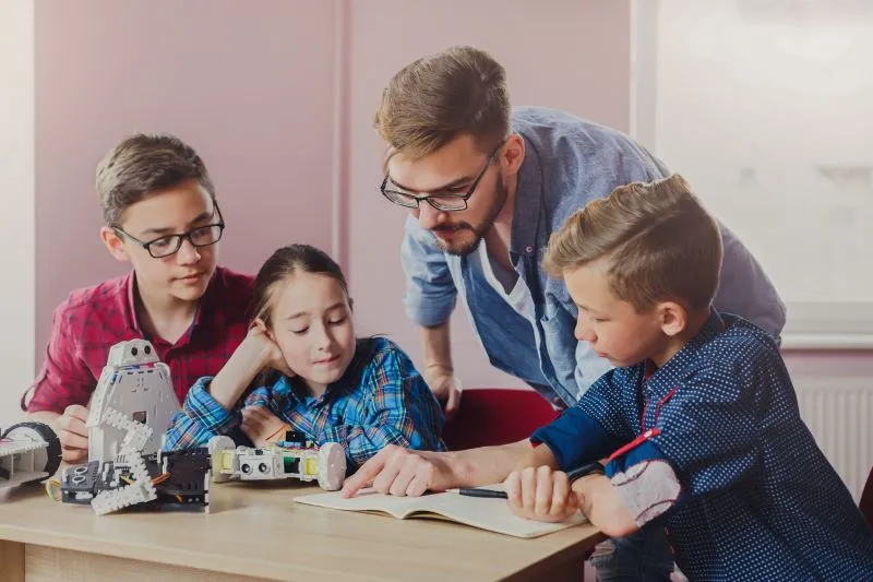 The use of differentiated instruction is visible in this collaborative robotics session. The teacher adapts the learning experience to meet the various needs of students, guiding them through the problem-solving process. By tailoring instruction to different learning styles, this approach ensures that all students, regardless of their background or skill level, can actively participate and succeed.