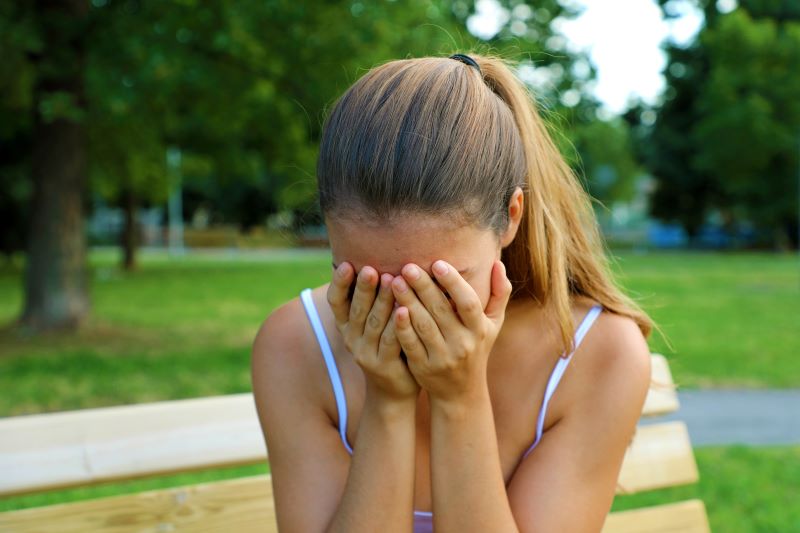 Girl is sitting outside and crying hidding her face with hands